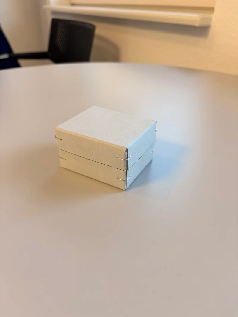 Geschlossene graue Kartonschachtel mit sichtbaren Heftklammern an den Ecken