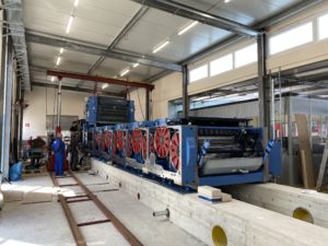 Blaue Druckmaschine von der hinteren Seite auf Betonfundament mit roter Walzenverkleidung in einer Produktionshalle von Hubert von Carnap